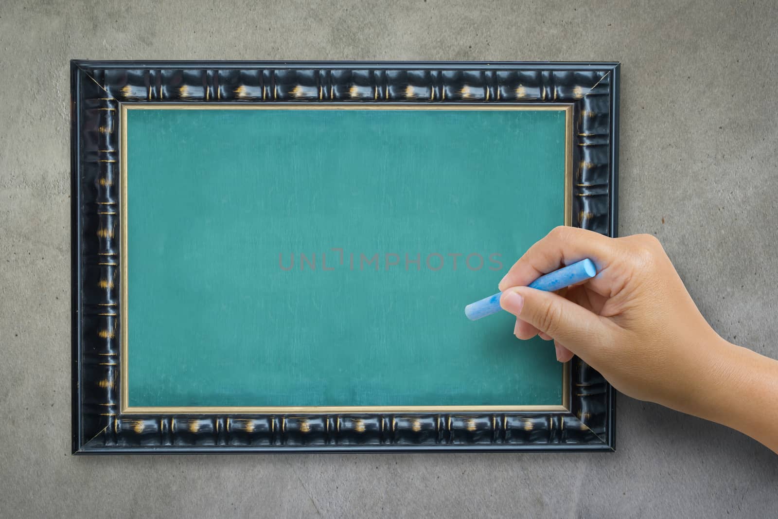 The hand that catches Chalk is preparing to write the alphabet on empty green chalkboard with black wooden frame on grunge cement wall, vintage wall texture background. 