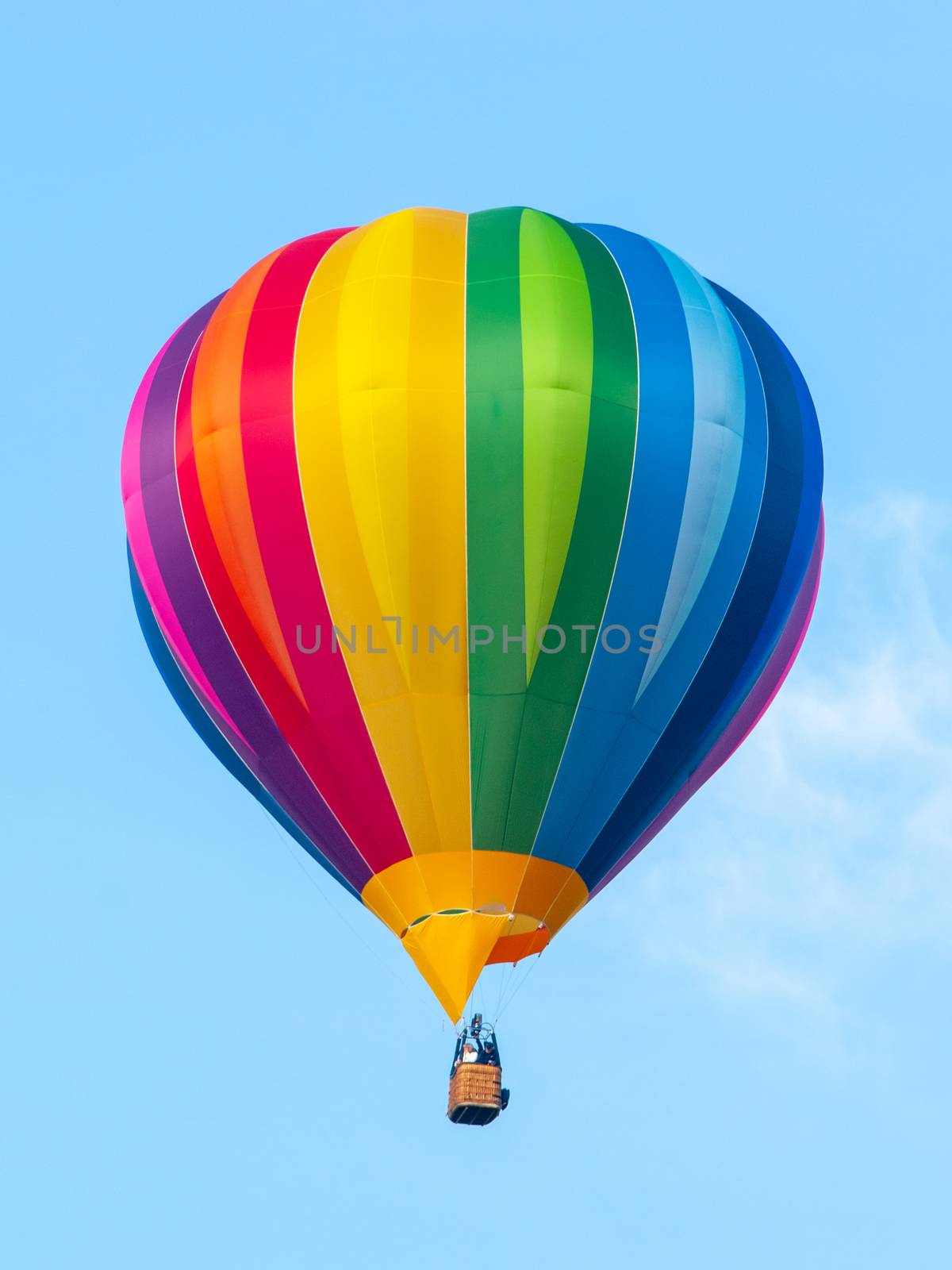 Hot air balloon in rainbow spectrum colors on blue sky background.
