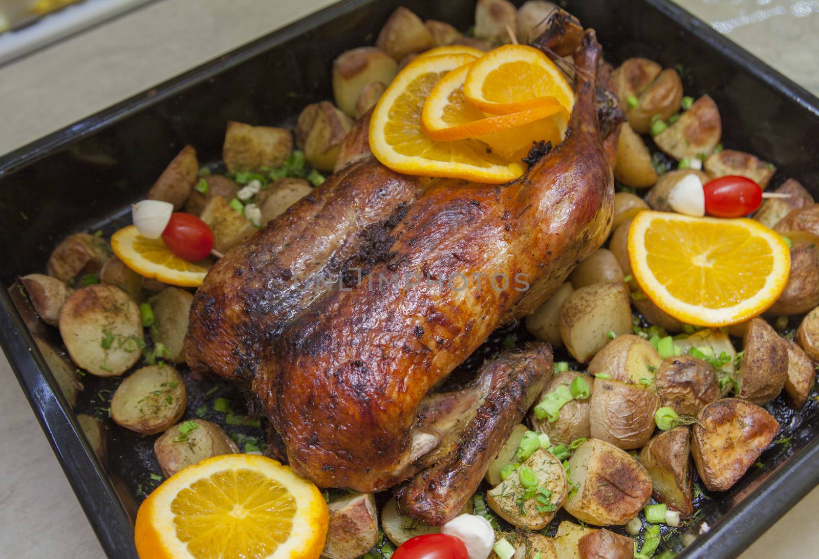 A pan with grilled duck, potatoes, oranges and fresh garlic.