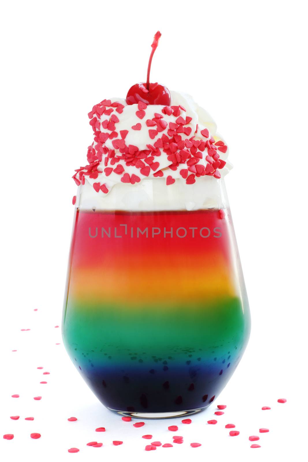 Rainbow colored jello dessert in glass with whipped cream, red candied cherry and heart shape confectionery on top isolated on white background, Valentines day