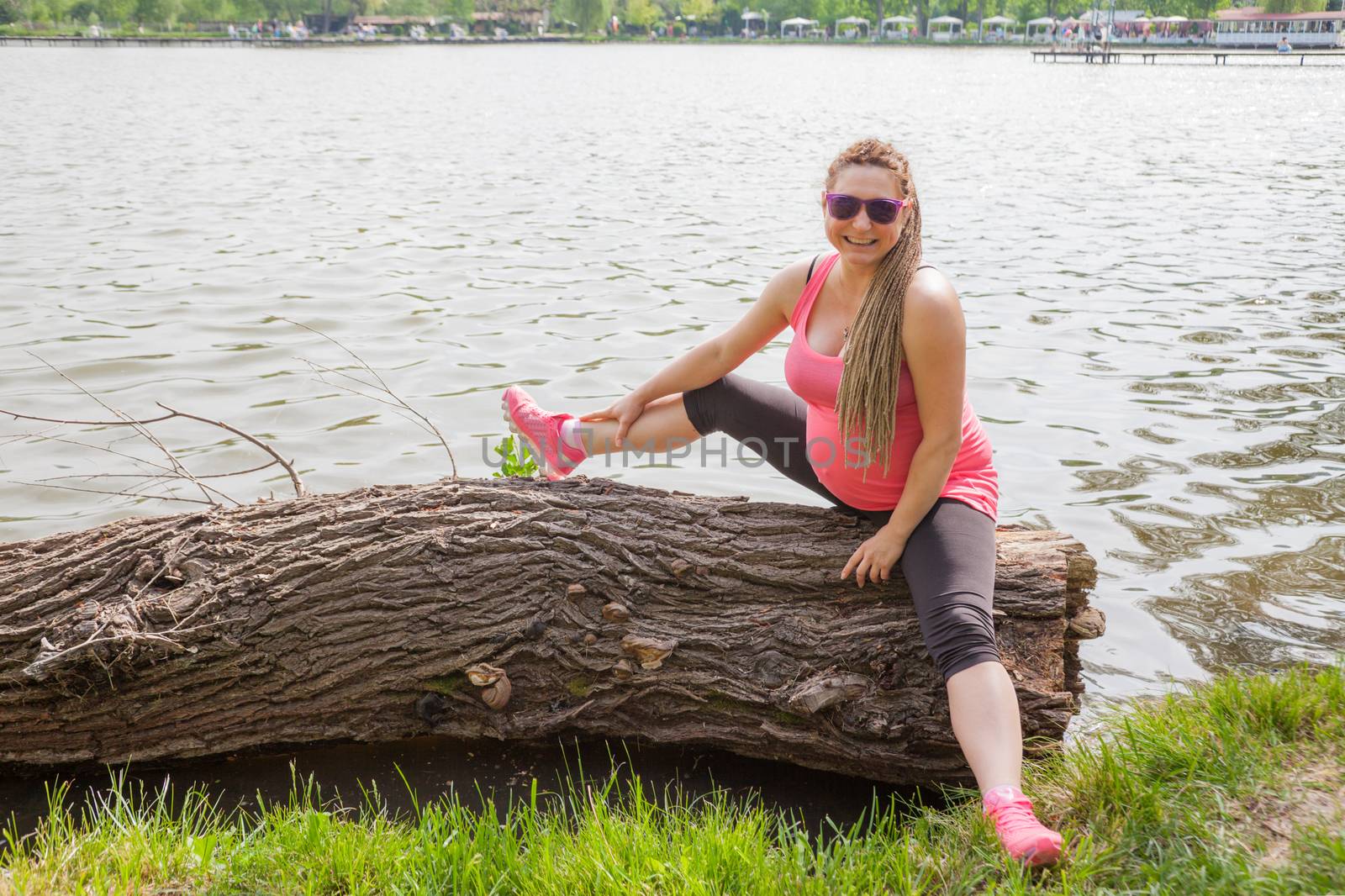 Pregnant woman stretching on a lag in front of a small dam smiling.