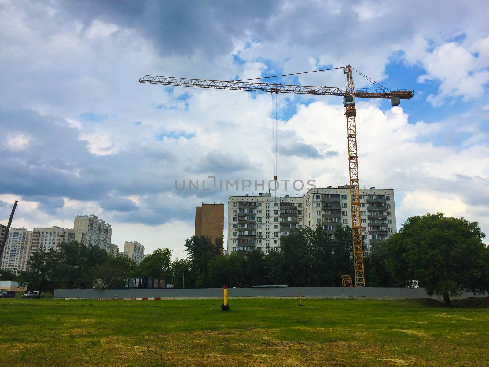 Construction crane on the background of a green grass house
