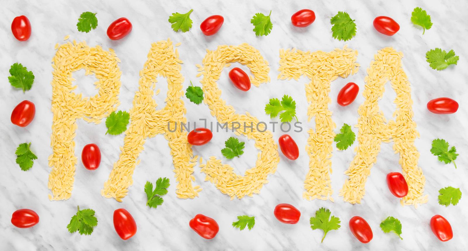 The word "PASTA" written with rice-shaped tiny Orzo pasta on marble background, decorated with tomatoes and coriander.
