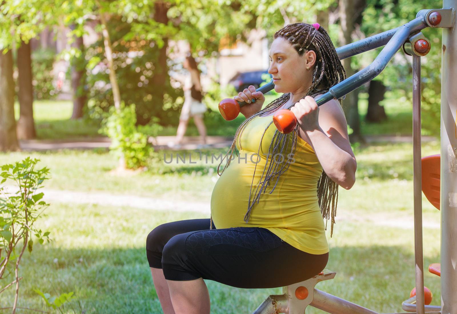 Pregnant woman exercising outdoors in public gym in the park.
