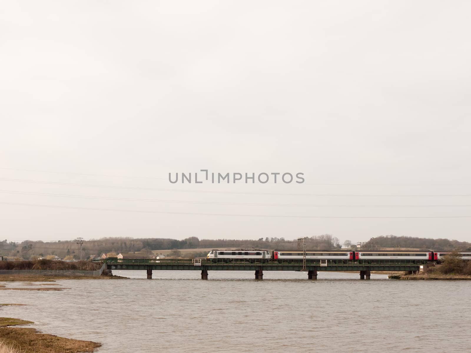 moving train blur motion on bridge across river large sky open space; essex; england; uk