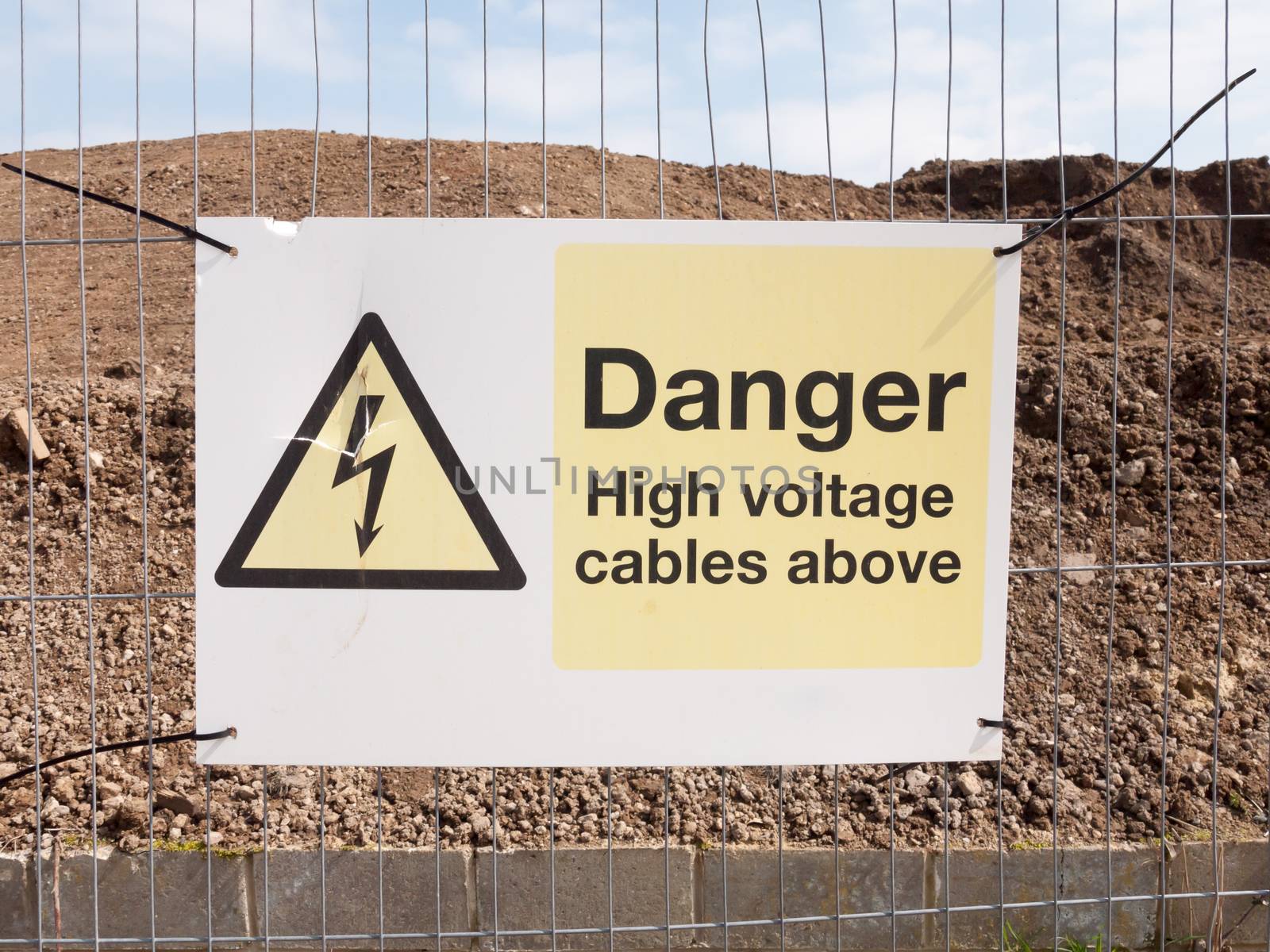 close up construction site fence sign: danger high voltage cables above by callumrc