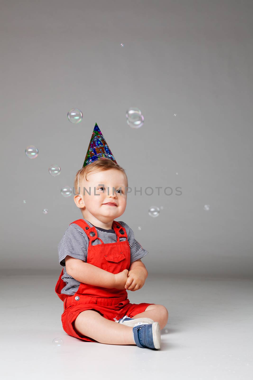 happy baby boy with birthday hat and foam balloons, studio shot