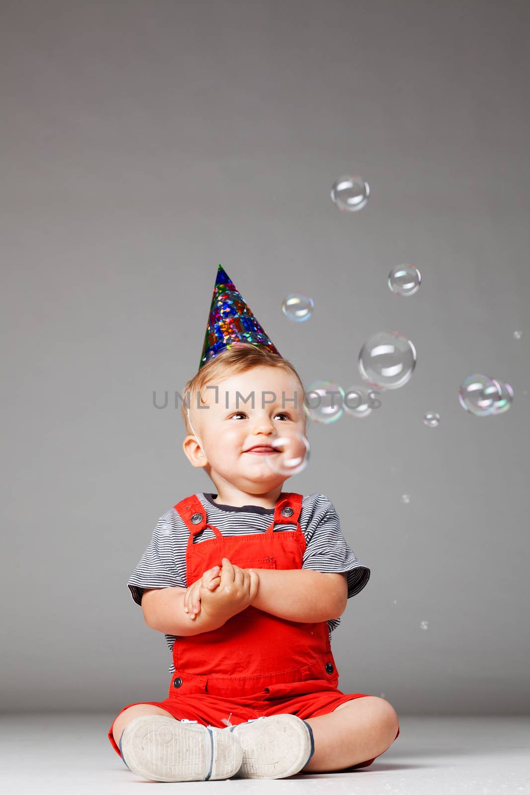 happy baby boy with birthday hat and foam balloons, studio shot