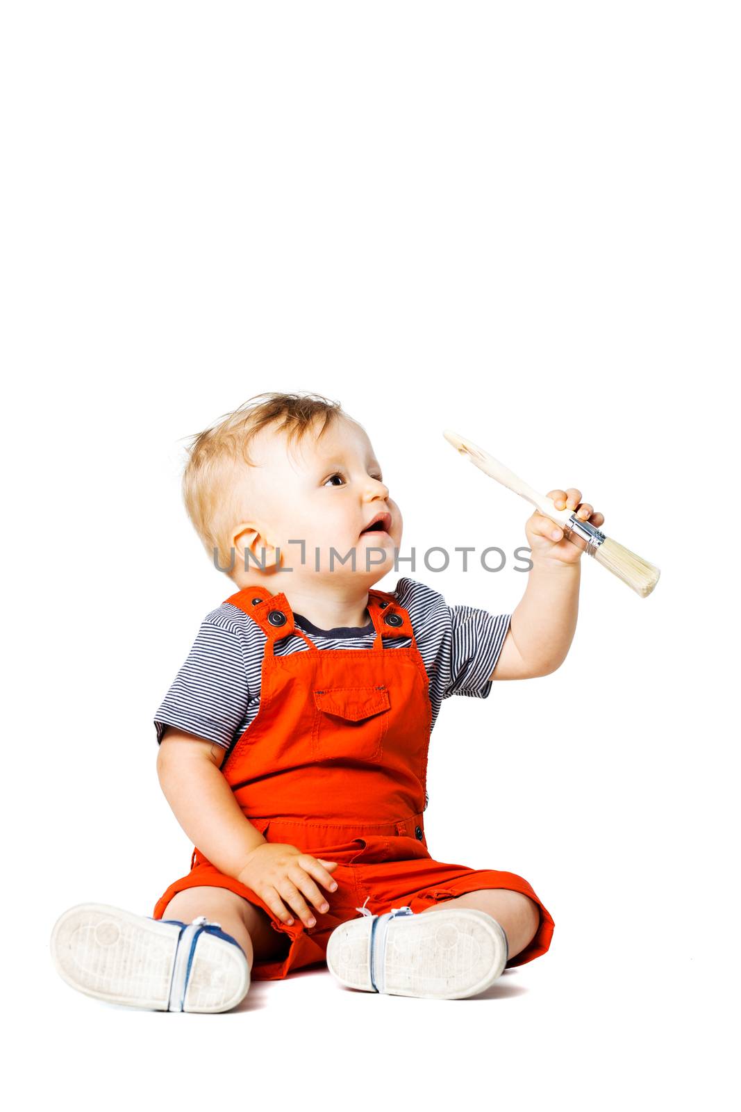 baby boy sitting on the floor, holding paint brush, isolated on white
