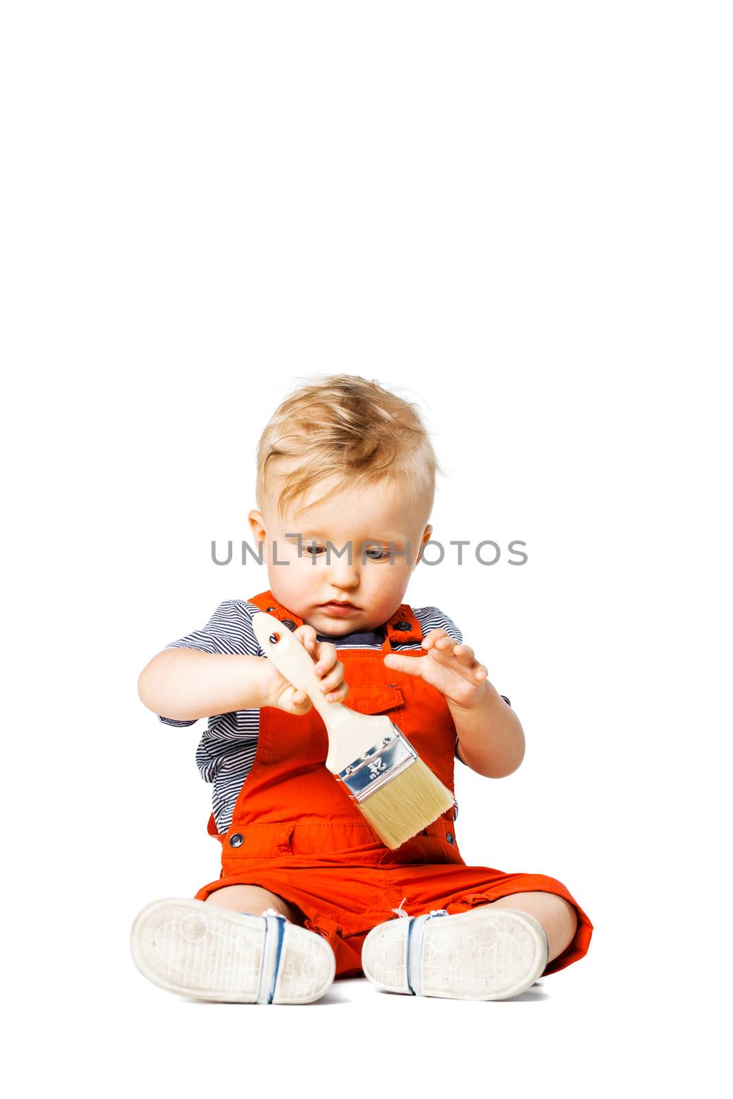 baby boy sitting on the floor, holding paint brush, isolated on white