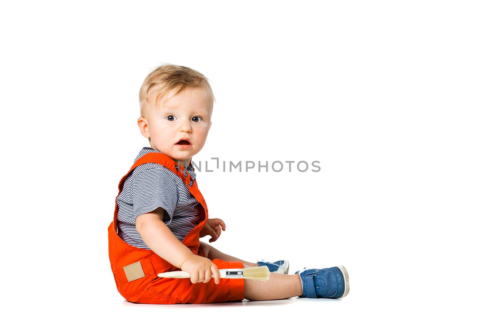 baby boy sitting on the floor, holding paint brush, isolated on white