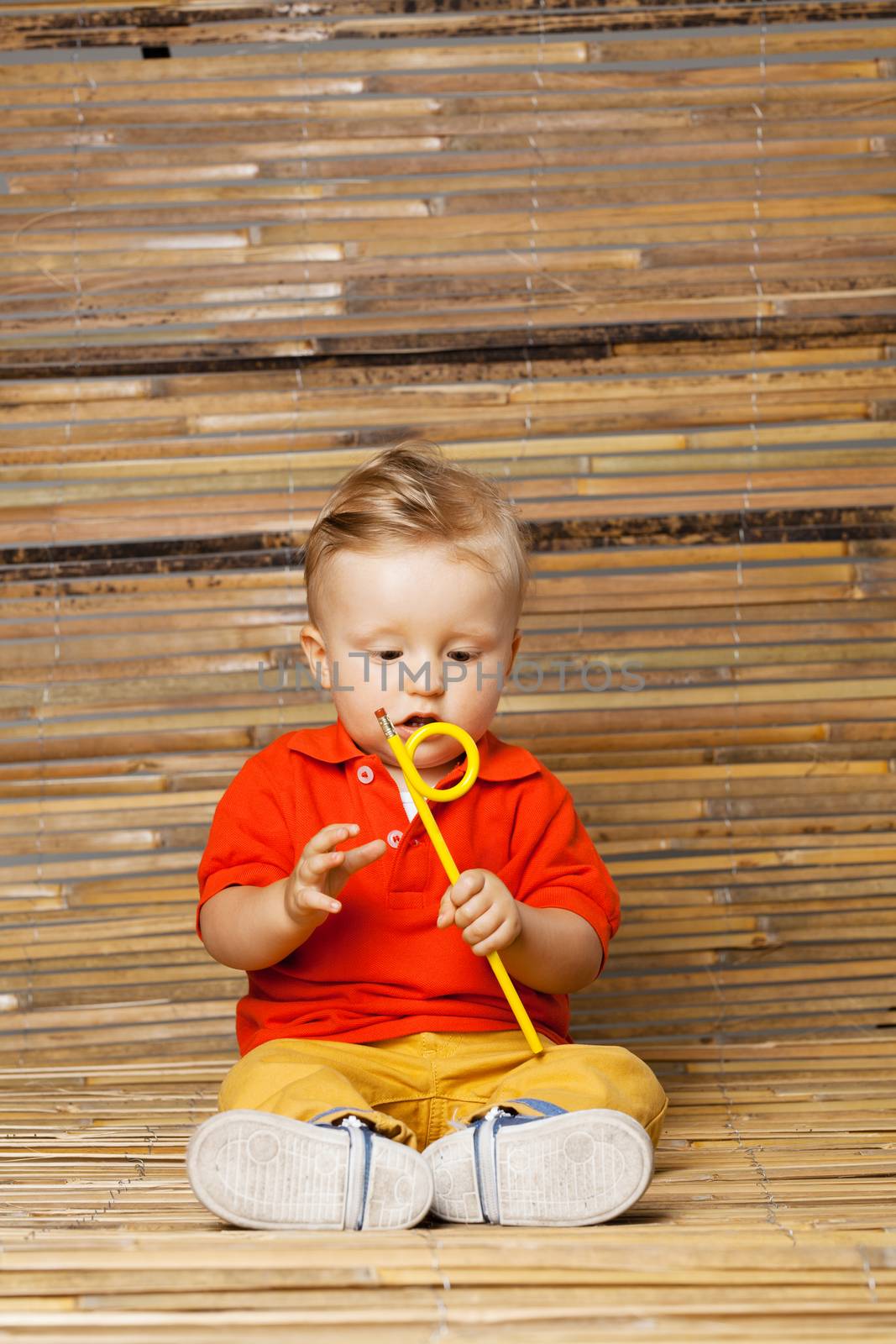 baby boy sitting on the floor, holding a pencil, on bamboo background