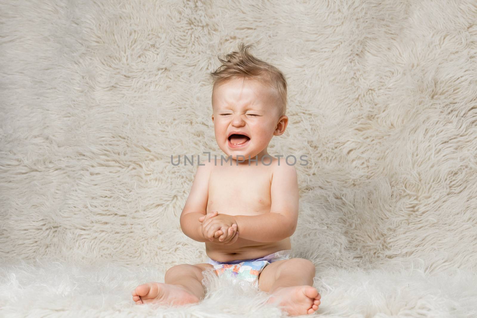 crying baby boy in diapers, sitting on a shaggy woolen homemade blanket
