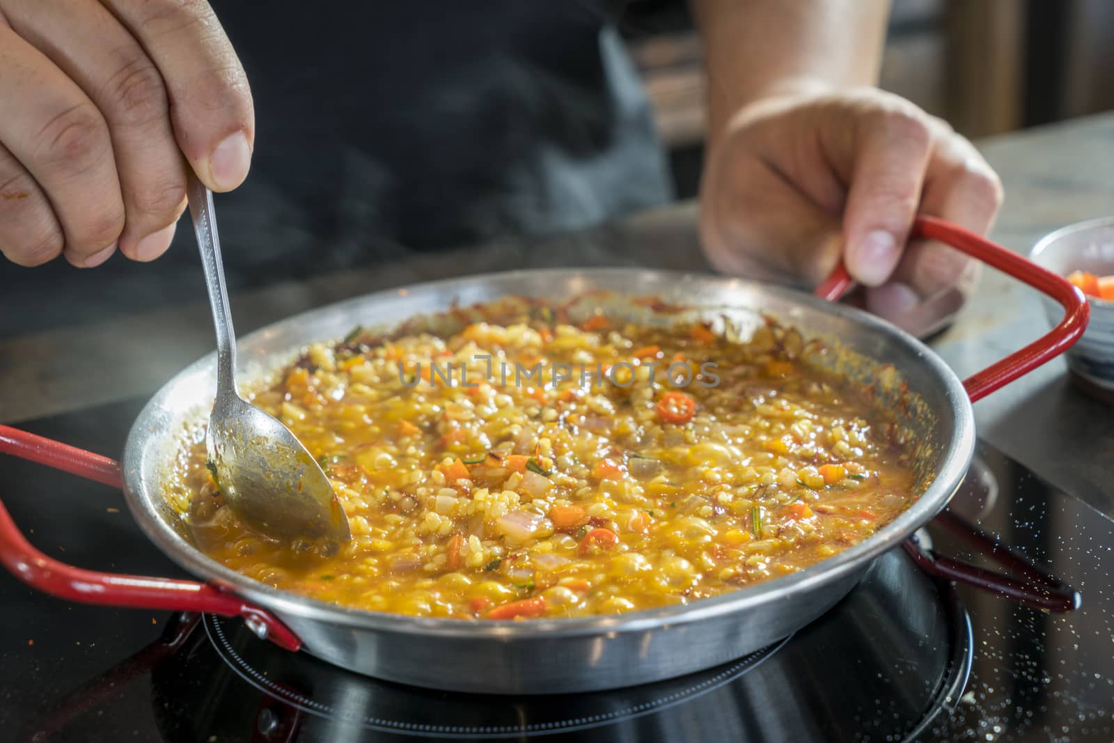 Chef is cooking paella with spoon, close up