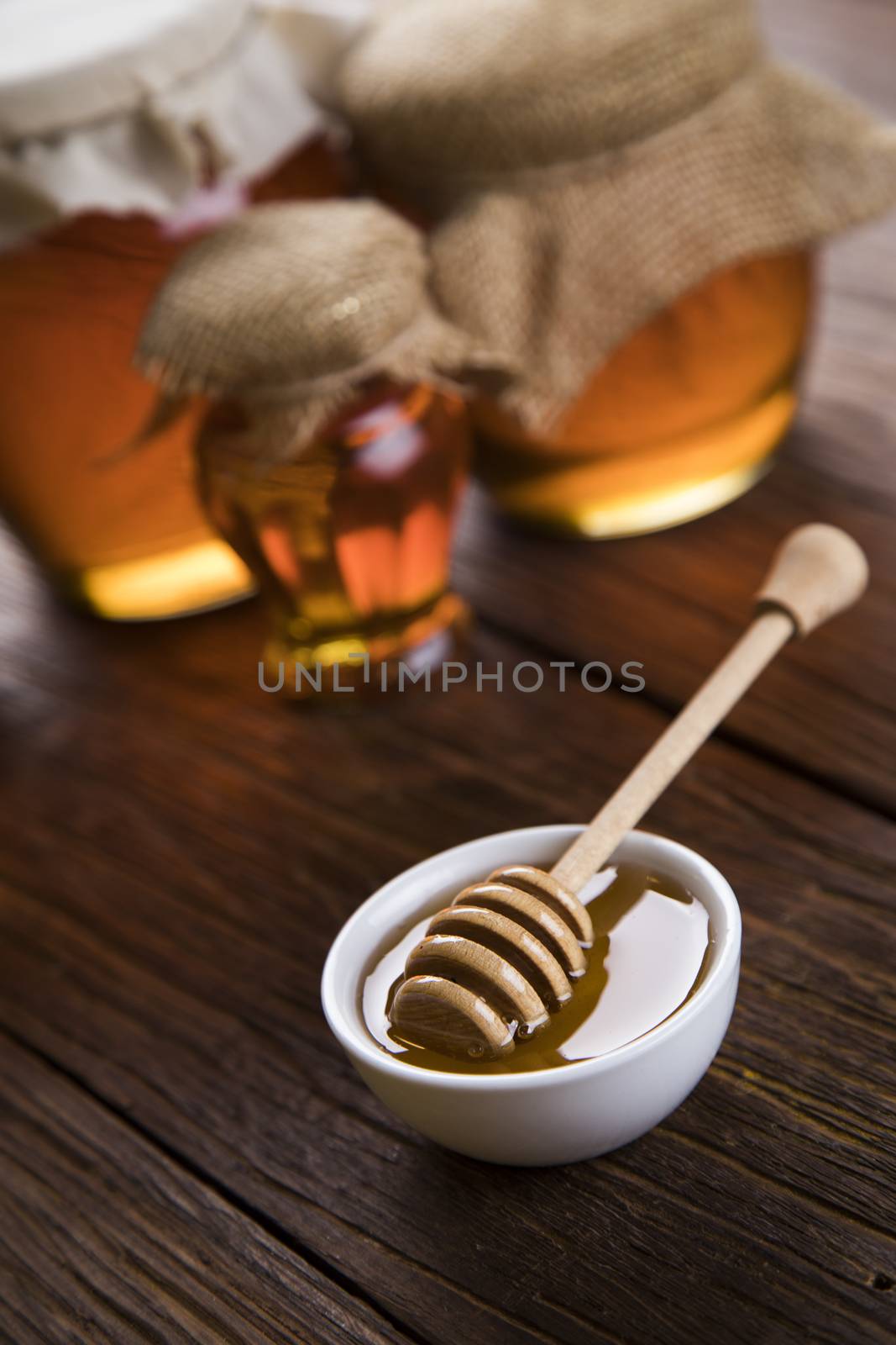 Honey dripping from a wooden honey dipper in a jar on wooden background