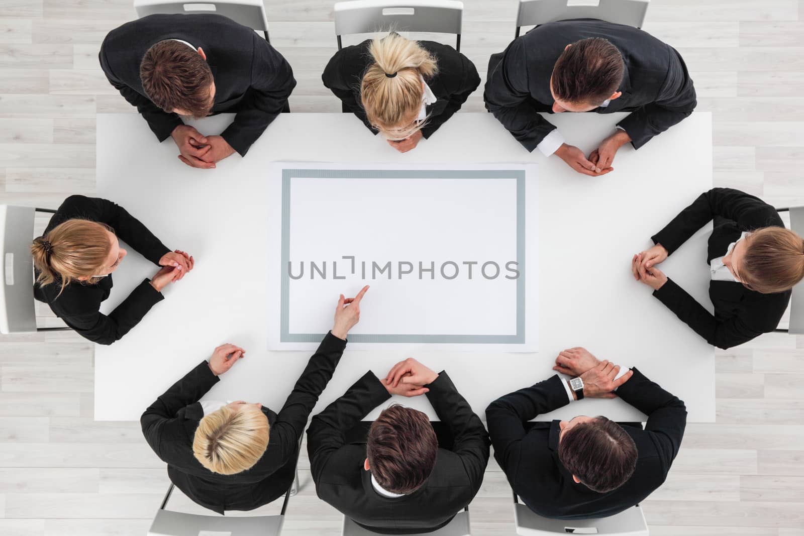 Business people sitting around empty table, business man pointing to blank copy space in the middle