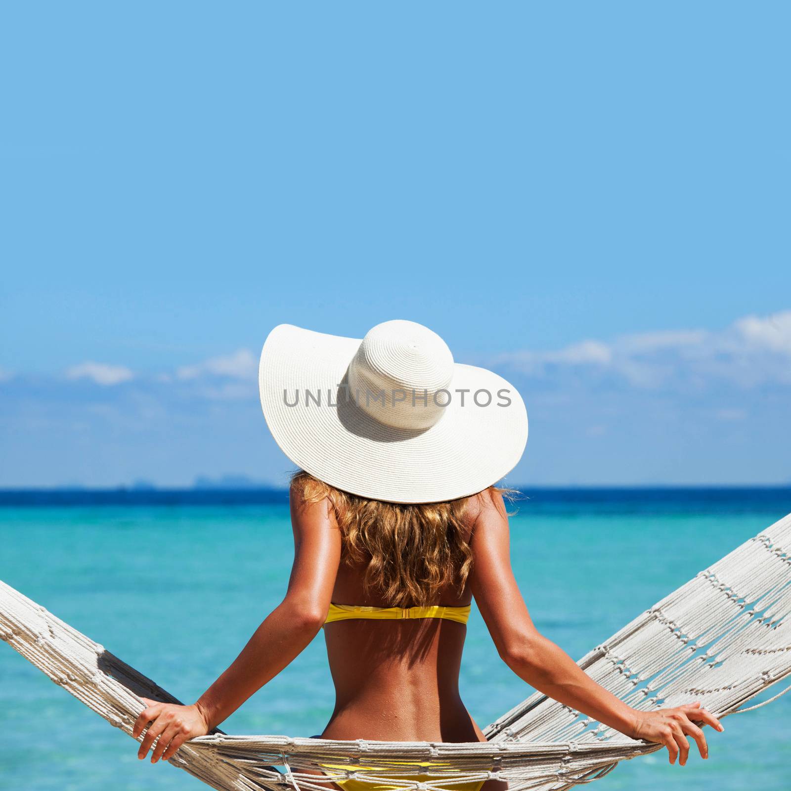 Woman in sunhat swinging in hummock on blue sea background