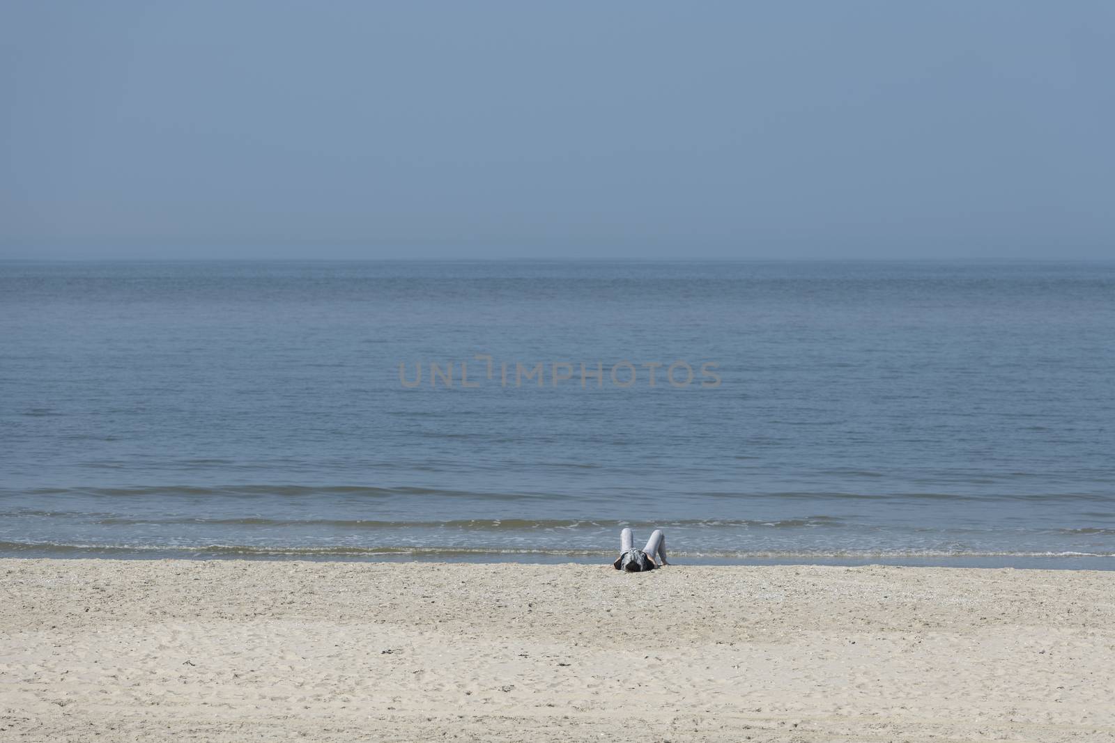 A single person who is sunbathing on the beach with the sea in the background
