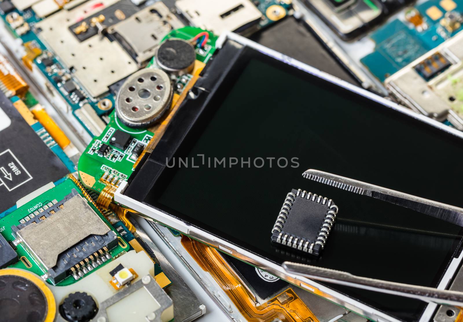 electronic chip and tweezers on background of the disassembled mobile phone