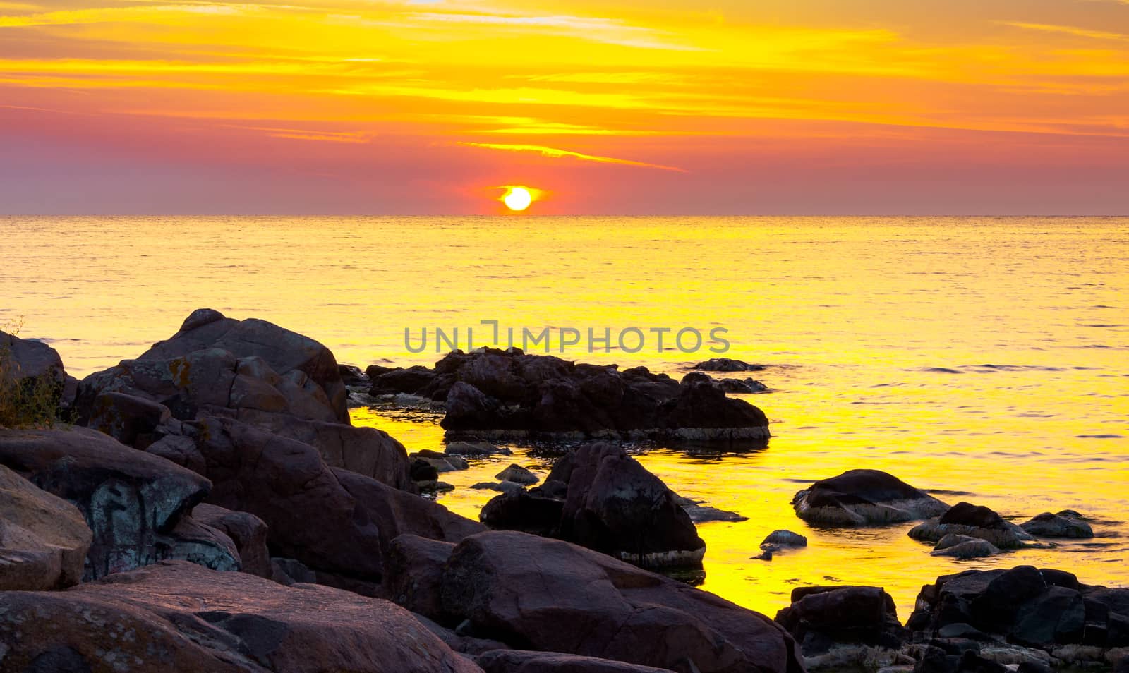 reddish sunrise over the sea with rocky shore by Pellinni