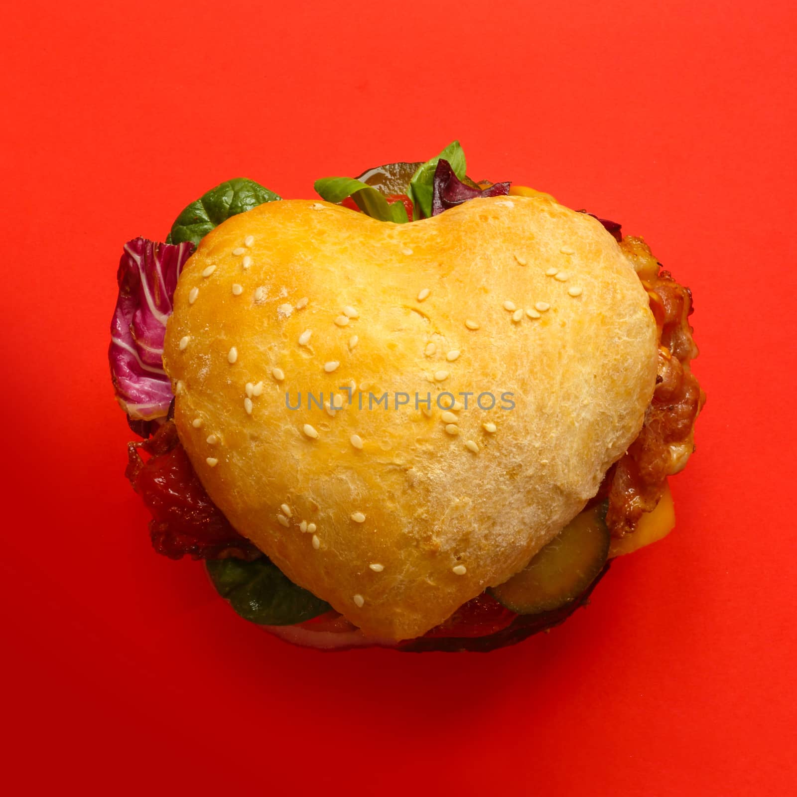 Heart shaped hamburger, love burger fast food concept, on red background, top view