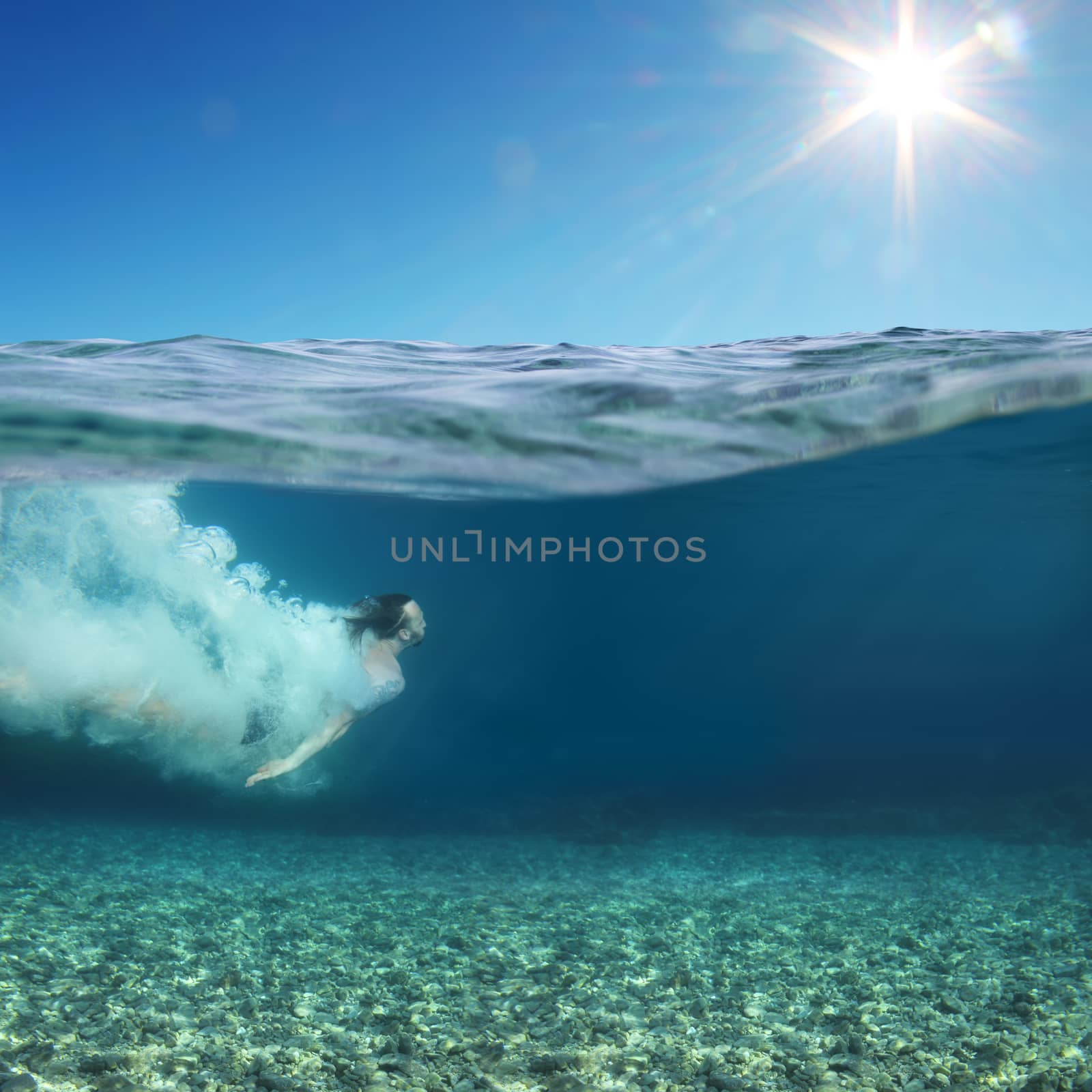 Man swimming underwater in blue transparent sea water under blue sky and sun