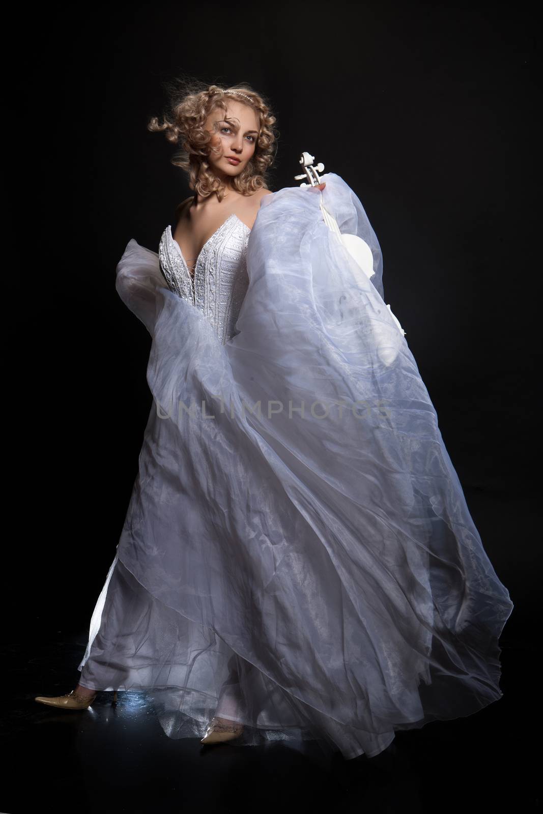 Young attractive woman in a wedding dress with a white violin on a studio background