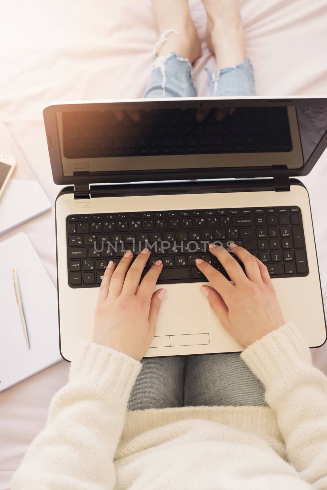 Young woman sitting in her bed and using laptop. Feminine workplace concept. Blogger working. Sun haze, glare.