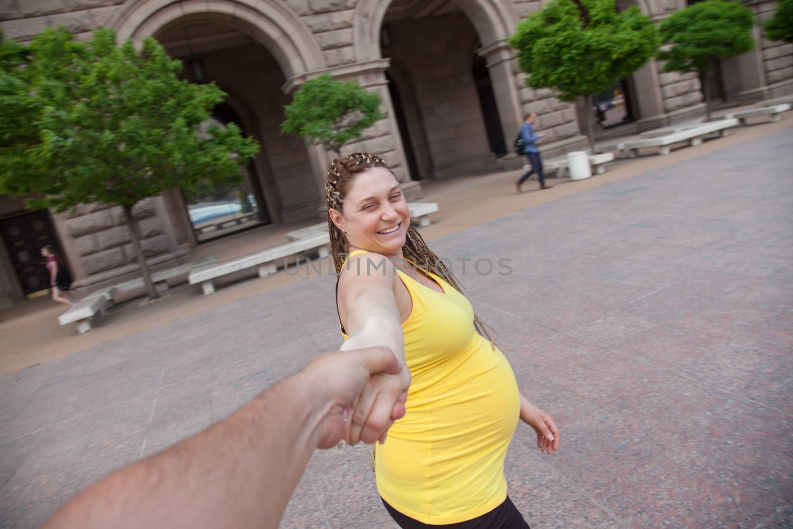 Laughing pregnant woman holding male hand is taking a walk outdoors.