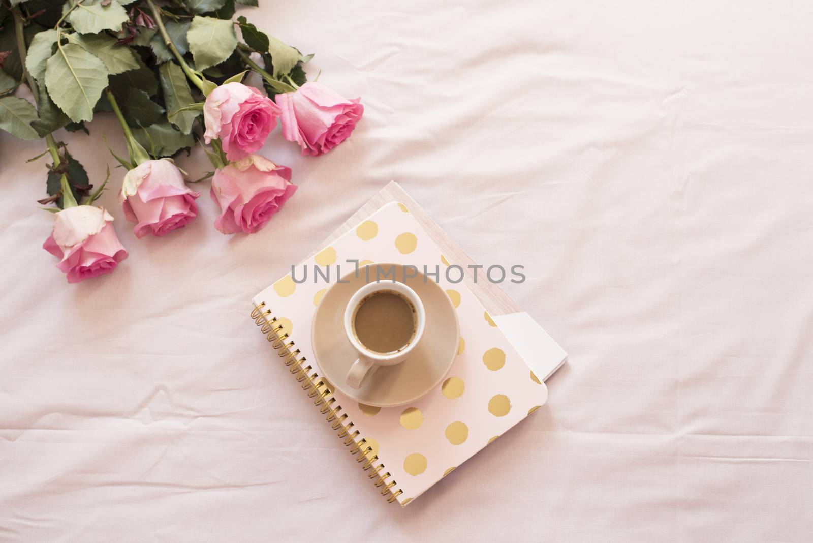 Coffee in bed on pink sheets. Roses, notebooks around. Freelance fashion home femininity workspace