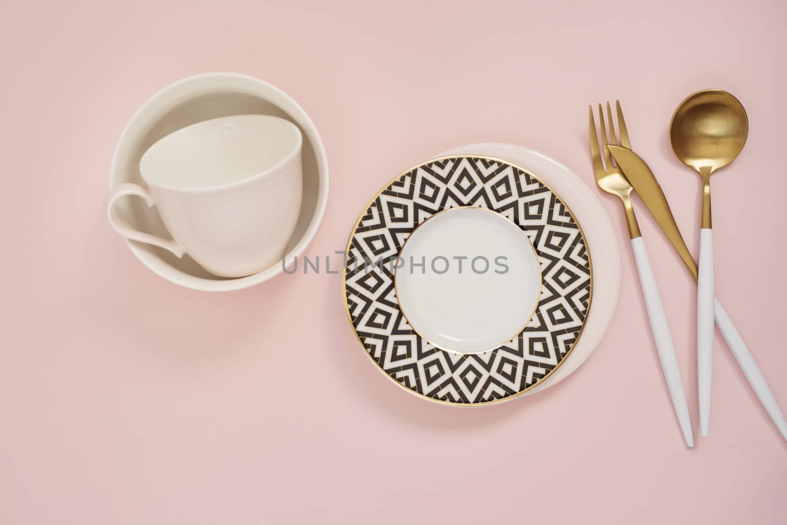 Gold cutlery. Golden spoon set, golden knife, spoon, fork, coffee cup and empty dishes on the table. Luxury spoon set top of view. Pastel punchy pink background