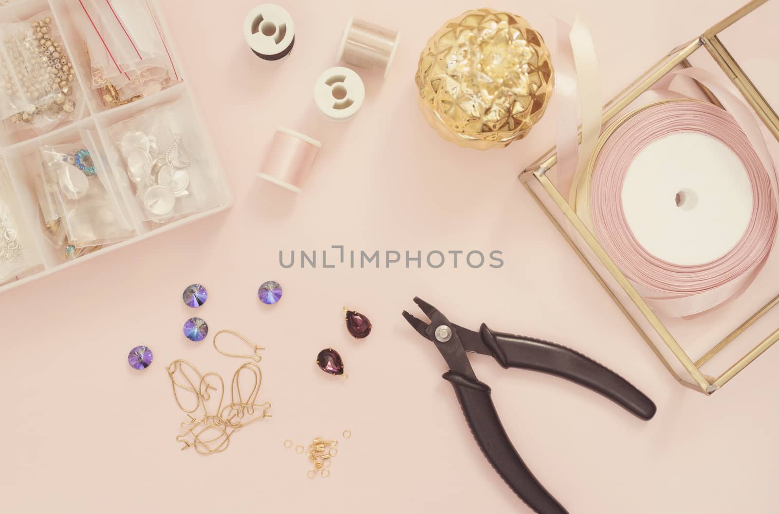 Jewelry designer workplace. Handmade, craft concept. Materials for making jewelry ? pliers, crystals? ear wires, ribbons. Freelance workspace in flat lay style. Pastel pink and gold.