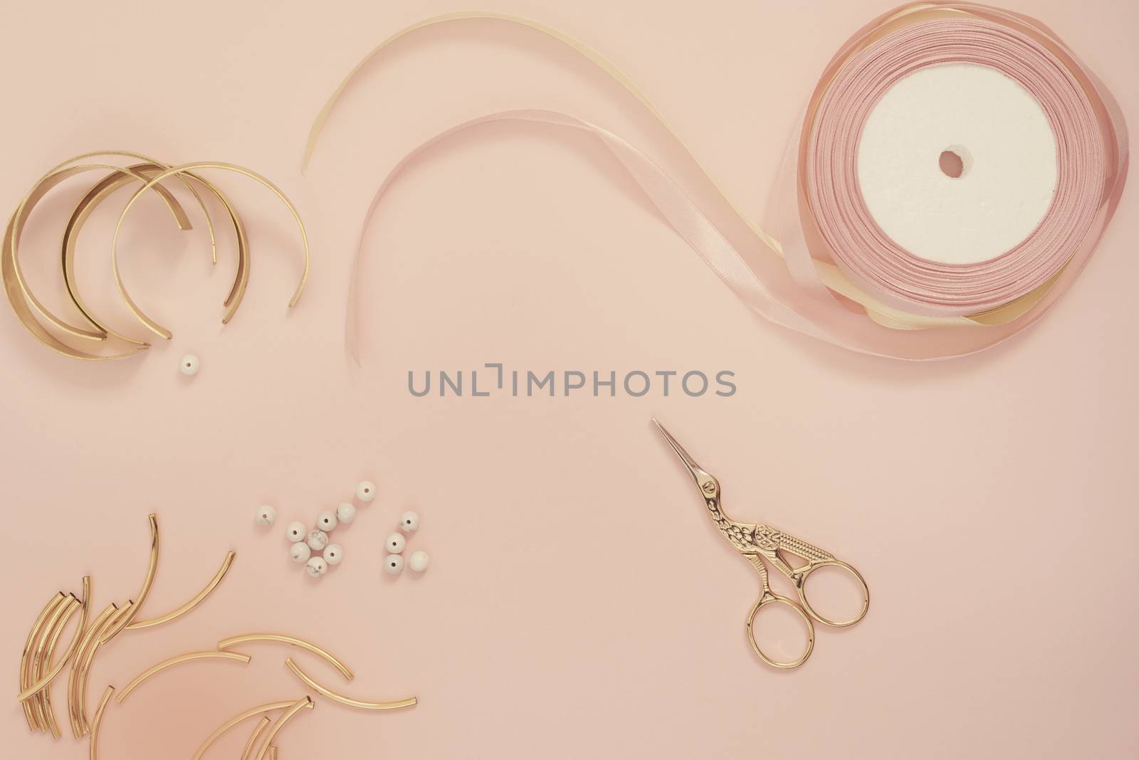 Jewelry designer workplace. Handmade, craft concept. Materials for making jewelry ? golden scissors, ribbons, gold tubes, bracelet settings. Freelance workspace in flat lay style. Pastel pink and gold