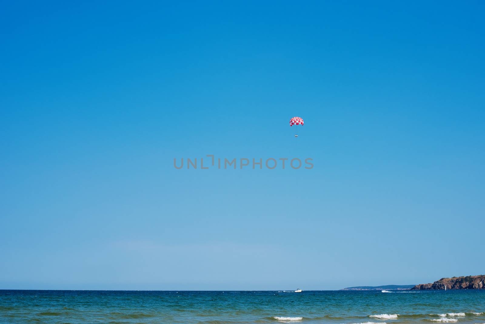 Parachuting over a sea, towing by a boat. Paragliding in the clear sky above the sea. Riding on a parachute behind a boat.