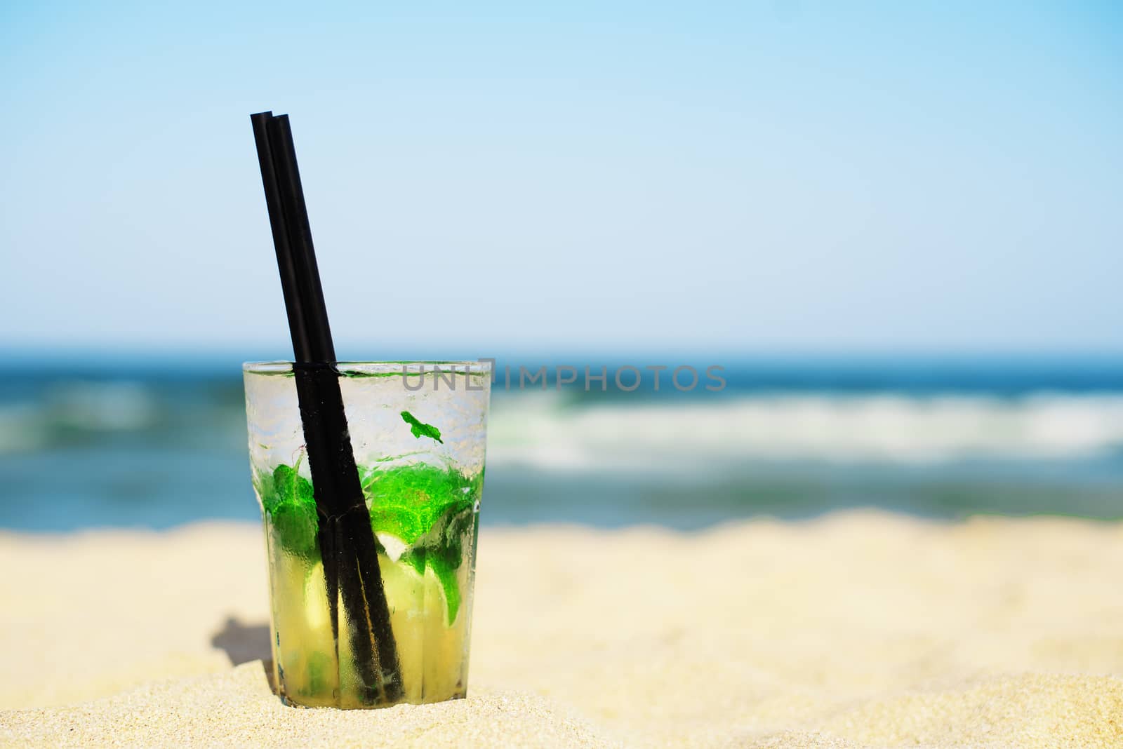 Mojito cocktail on the beach, blurred beach background. Sun, sun haze, glare