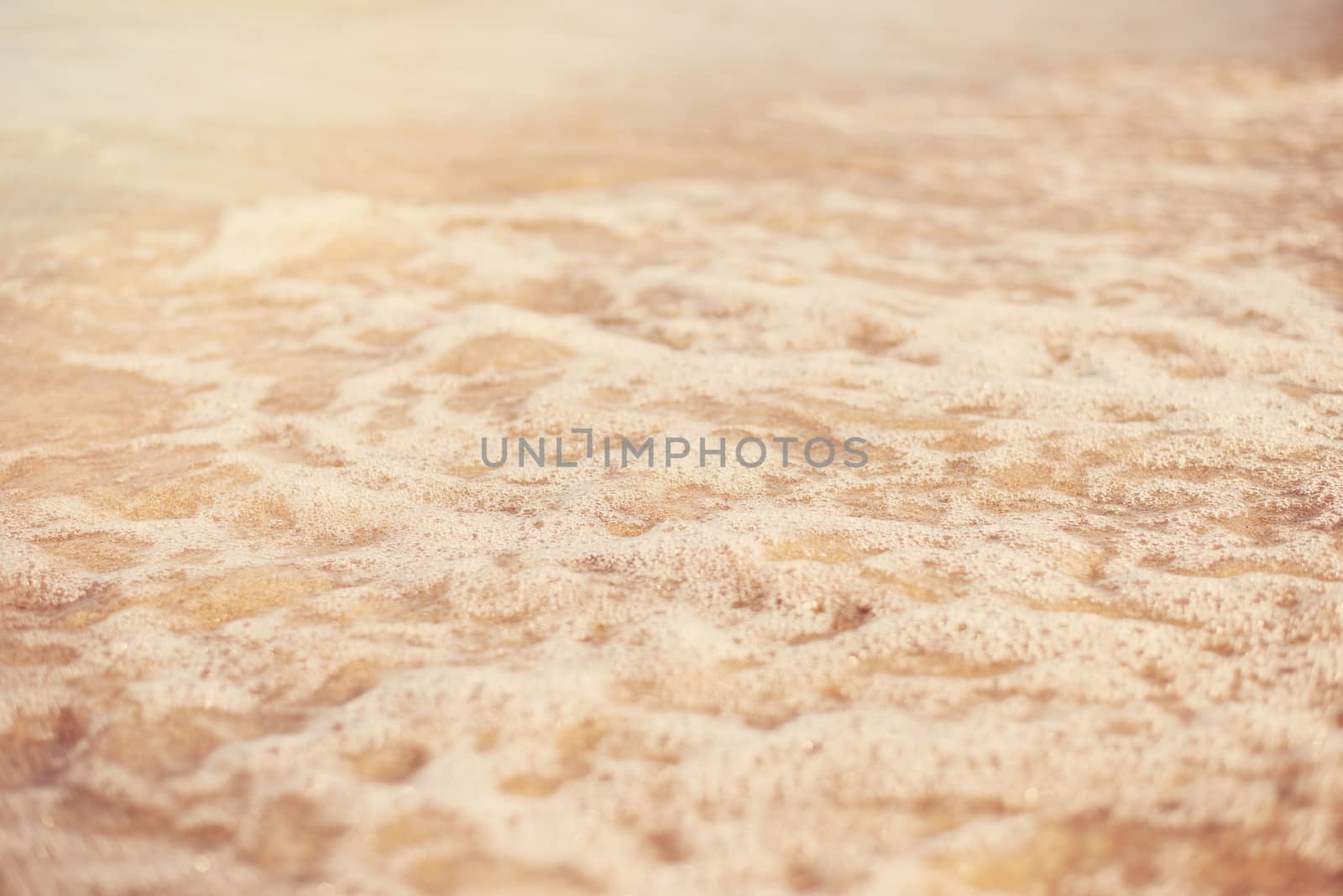 Sand and wave background. Soft wave of the turquoise sea on the sandy beach. Natural summer beach background with copy space. Sun, sun haze, glare