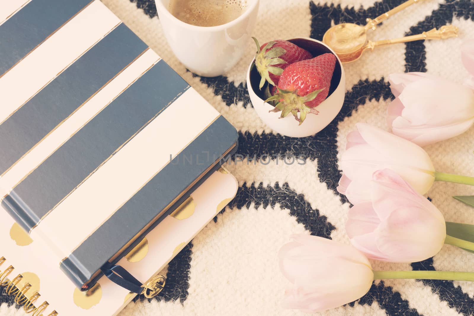 Coffee, strawberries, notebooks on Scandinavian rug. Pink Tulips and Gold Spoons. White black pattern and gold theme. Lifestyle concept