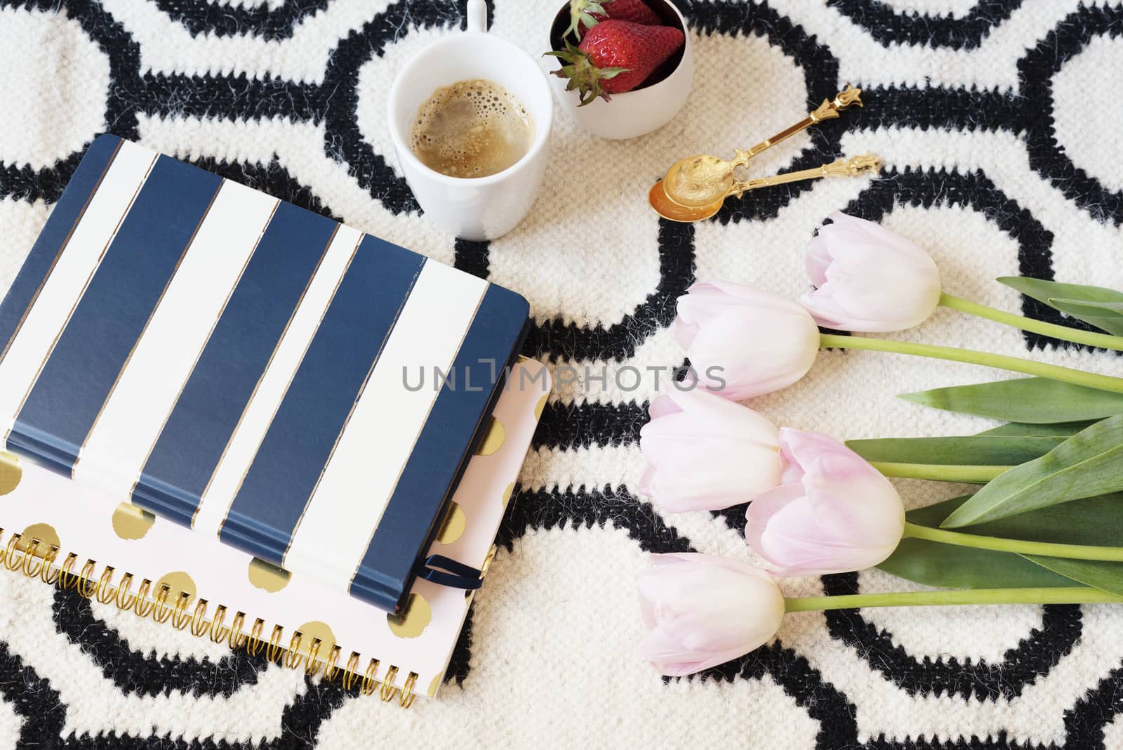 Coffee, strawberries, notebooks on Scandinavian rug. Pink Tulips and Gold Spoons. White black pattern and gold theme. Lifestyle concept