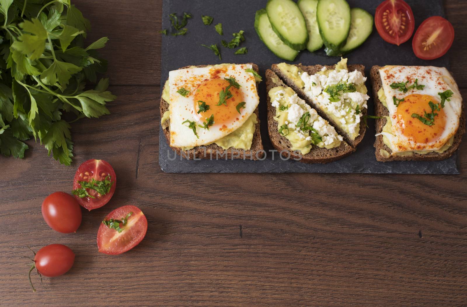 Avocado Toast. Healthy Breakfast. Top View. Homemade Sandwich With Avocado And Fried Eggs, Cherry Tomato And Cucumbers On A Wooden Background. Dark Food Photography