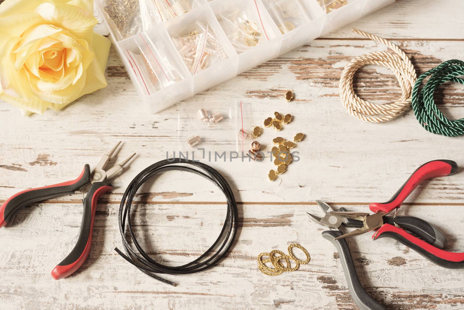 Workspace with tools for making jewelry - pliers, leather, earrings and bracelets, necklace. Kraft tools. Bright rustic wooden desk, table