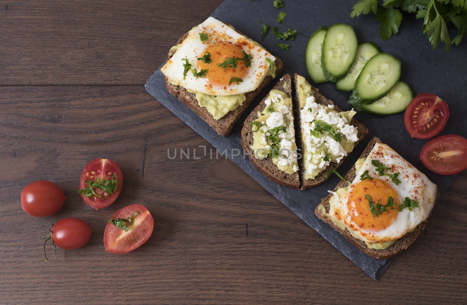 Avocado Toast. Healthy Breakfast. Top View. Homemade Sandwich With Avocado And Fried Eggs, Cherry Tomato And Cucumbers On A Wooden Background. Dark Food Photography
