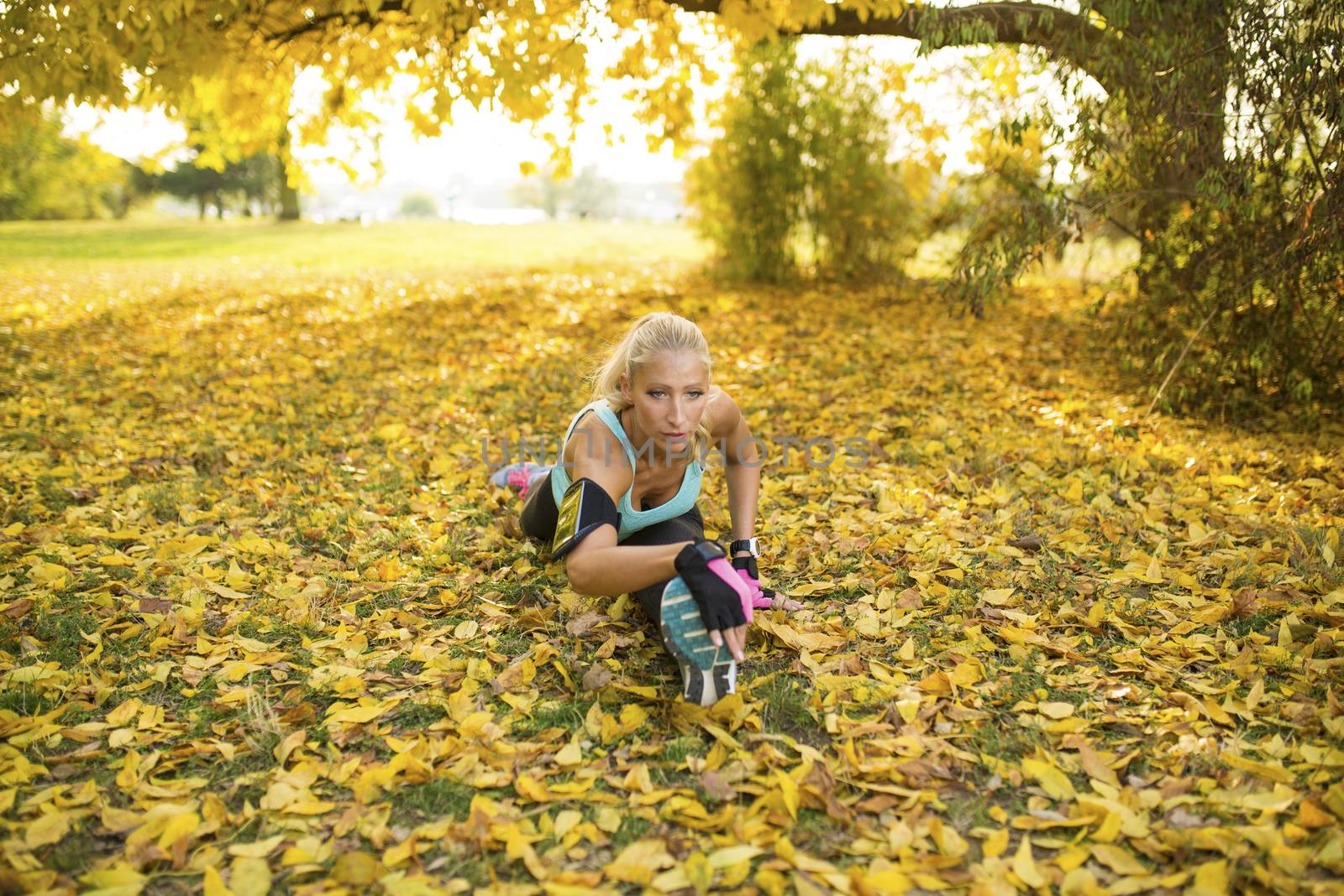 Attractive sporty blonde making split and exercising on the ground in the public park covered with a yellow leaves.