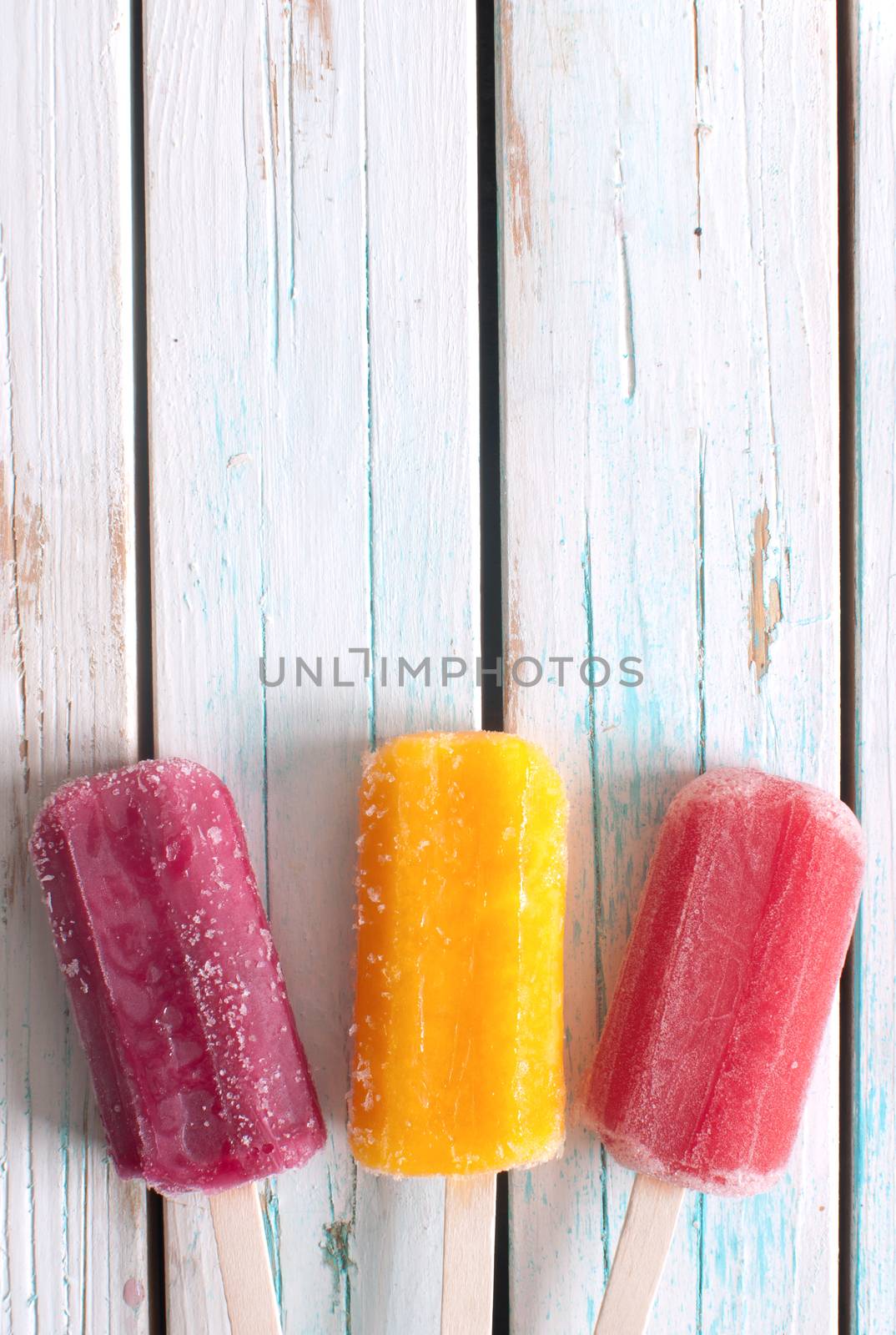 Frozen ice popsicles various flavors on wooden background with space
