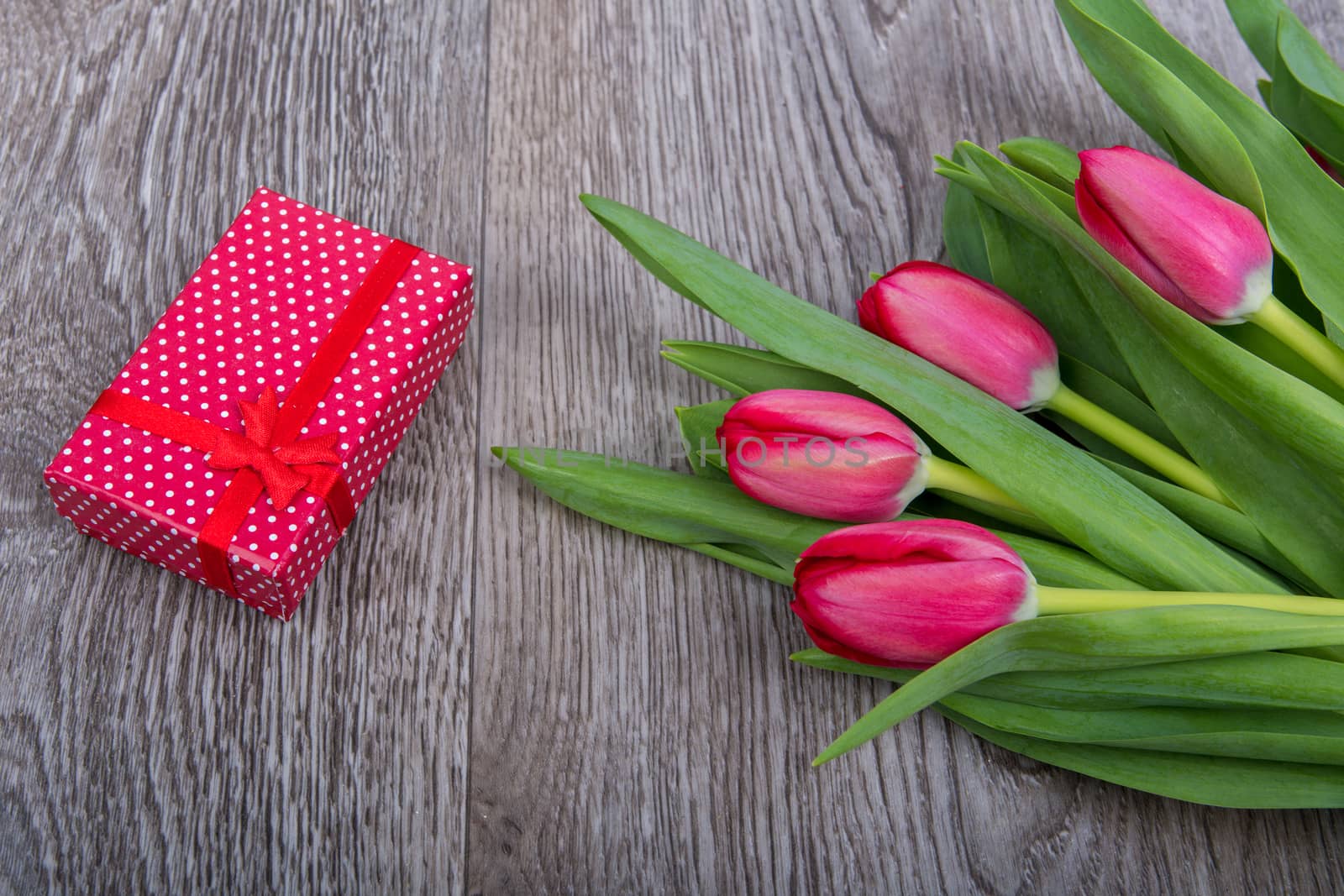 Red tulips and red gift on a wooden table
