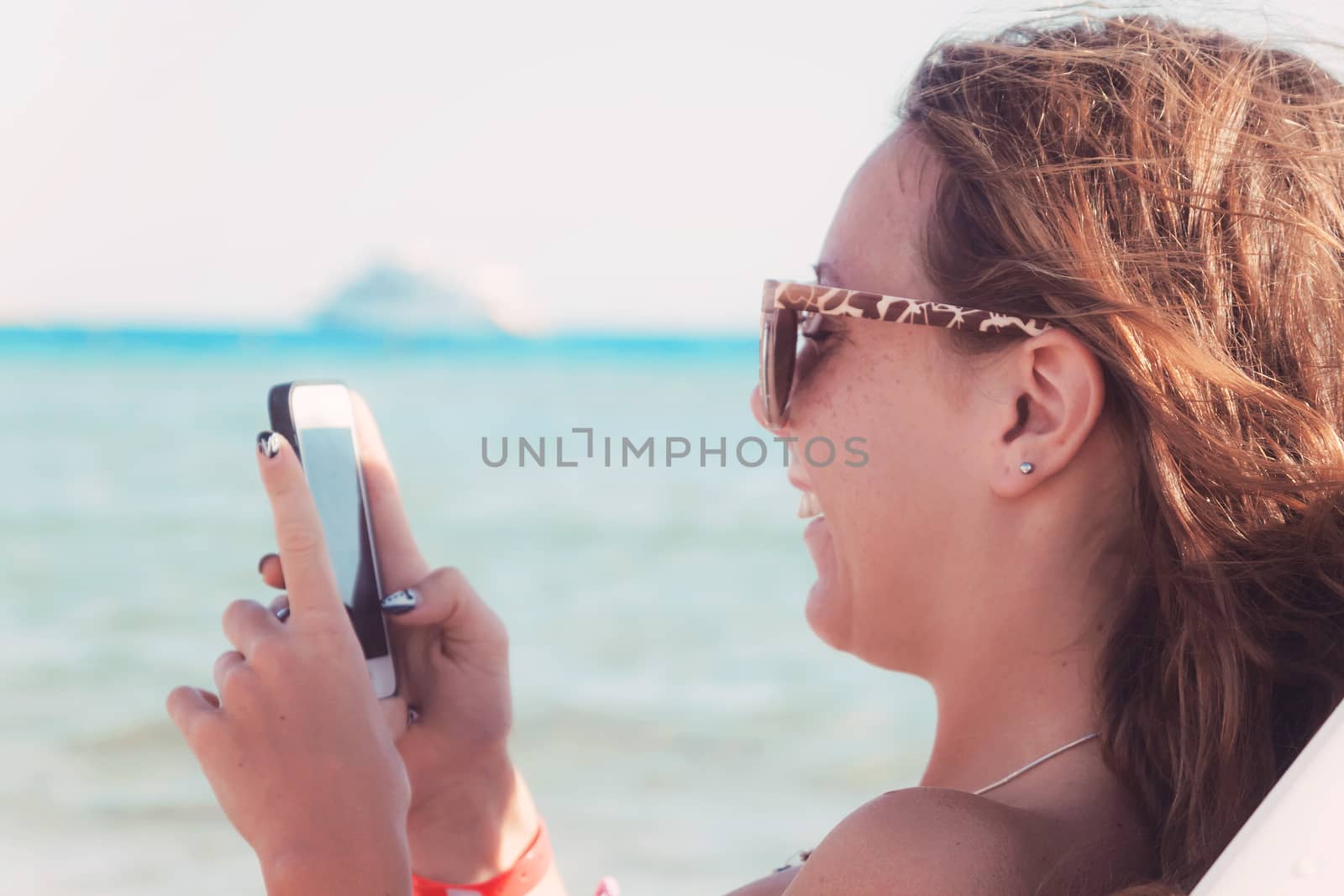 A young tanned woman looks and laughs into a smartphone through  by Tanacha