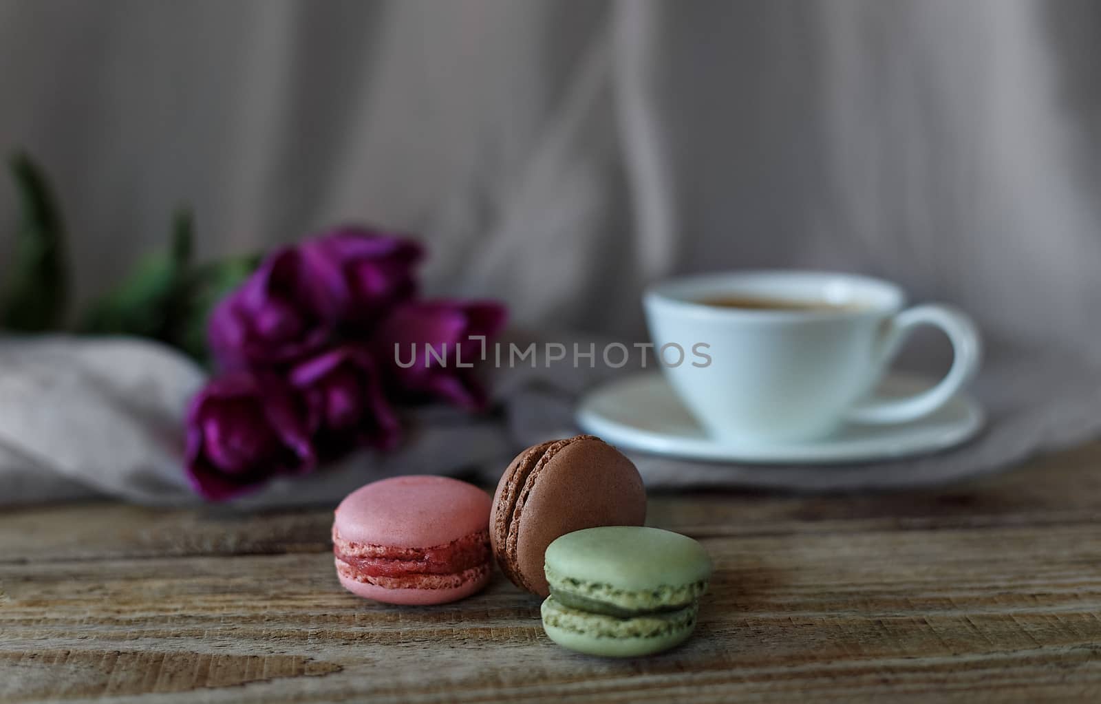 Macaroon biscuits on a wooden background with flowers and a cup of coffee