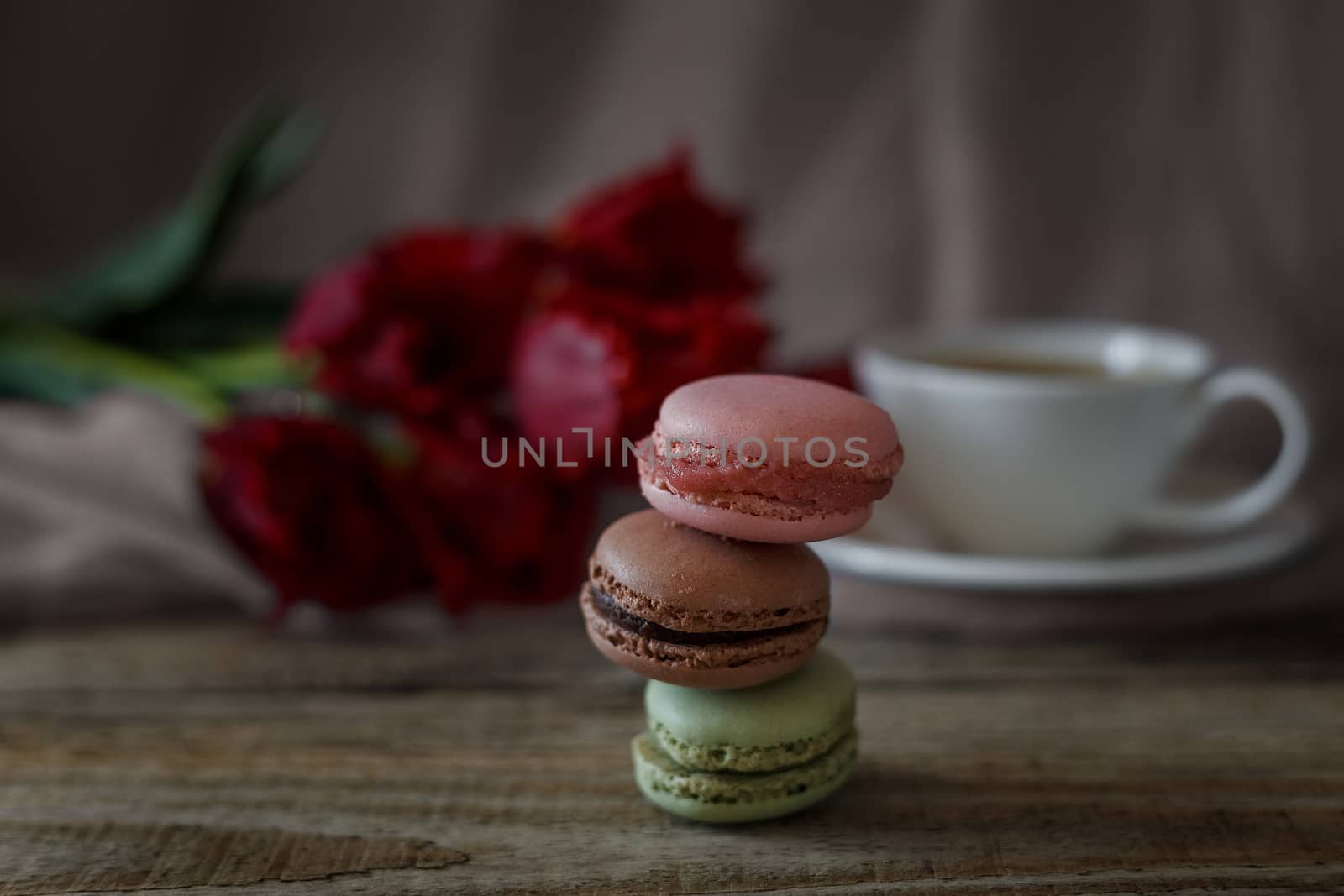 Macaroon biscuits on a wooden background with flowers and a cup of coffee