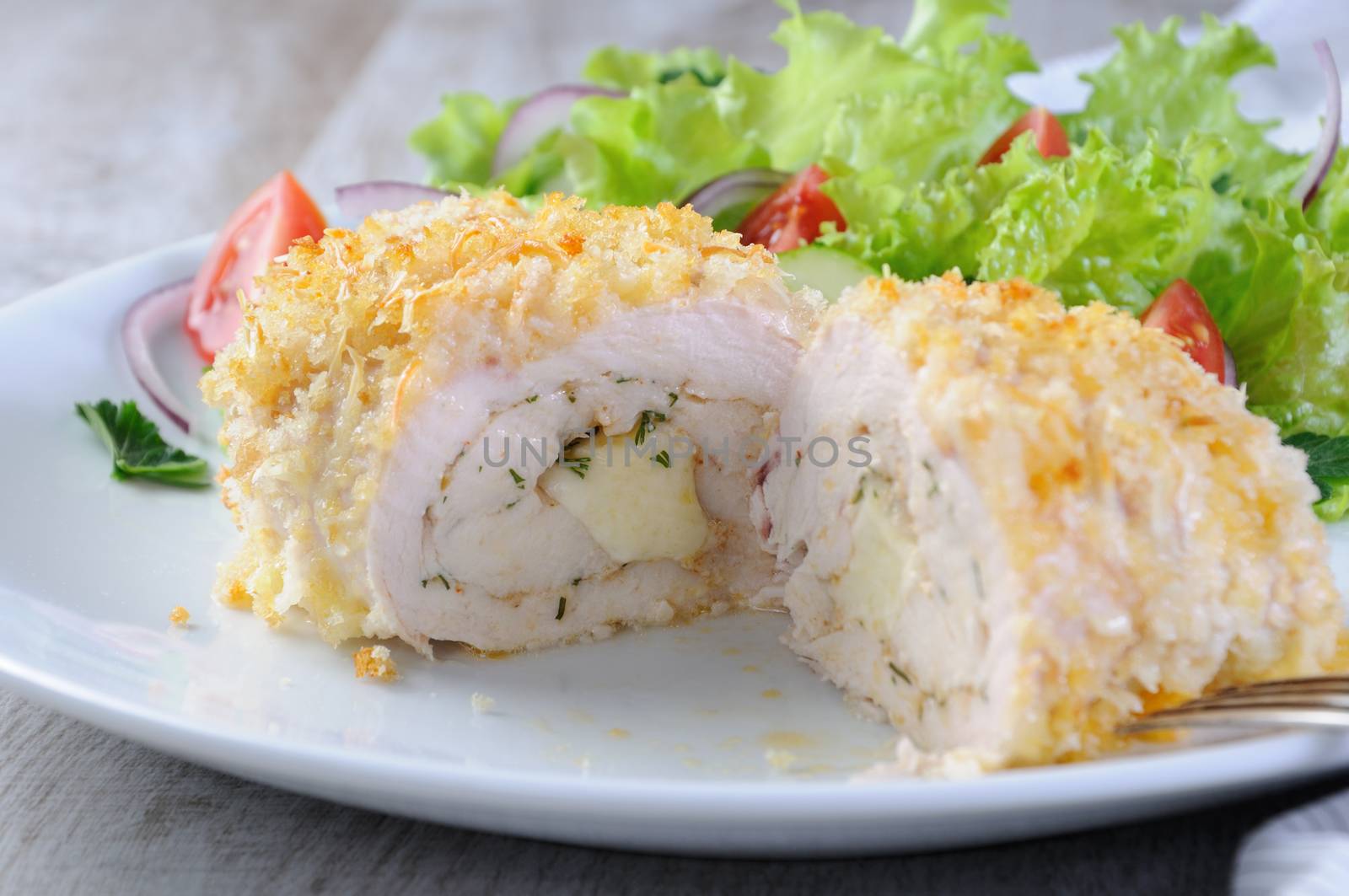 Sliced baked until golden, crispy crust chicken roll in breadcrumbs with Parmesan cheese, stuffed with cheese with herbs and garnish of vegetables.