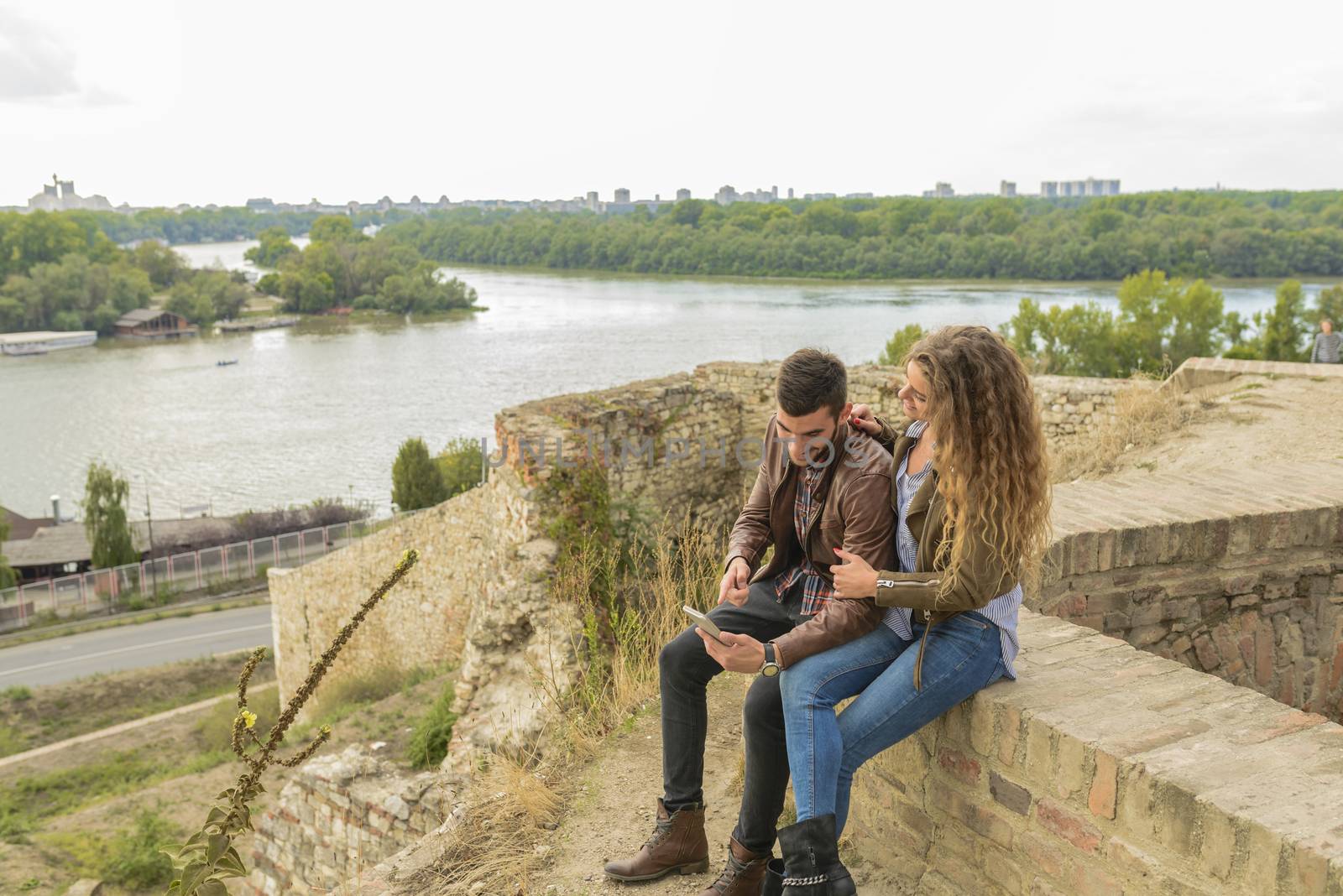 Modern young couple using their mobile phone near the river by VeraAgency