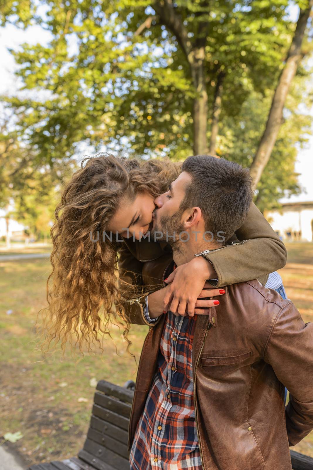 Attractive long haired girl is hugging his boyfriend while he is kissing her in the public park